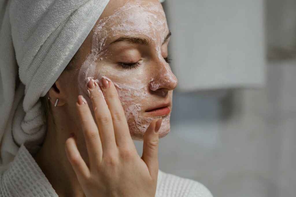 A woman applying a clay mask as part of her self-care beauty regimen indoors.