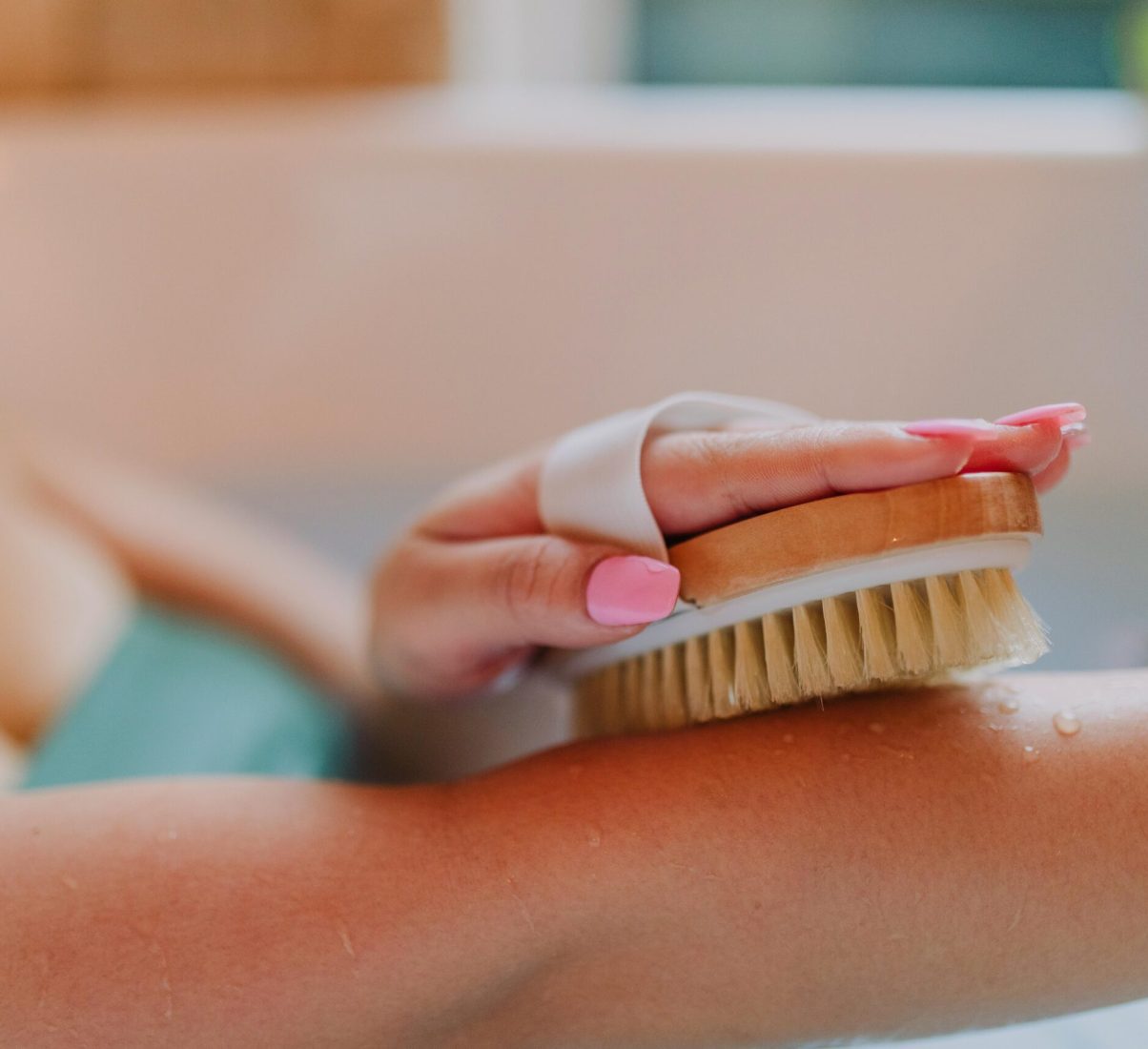 Close-up of a hand using a dry brush on an arm in a relaxing bath setting.